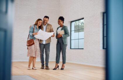 Happy couple of real estate buyers examining blueprints with their agent. Copy space.